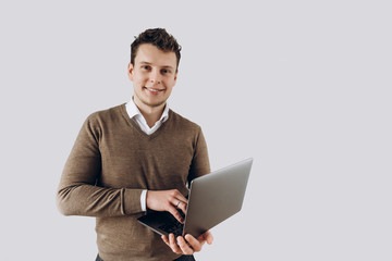 Young smiling guy with laptop in hands stands on white wall background on which there is space for text