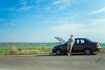 young man stands near broken car