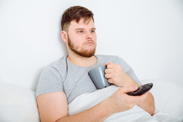 man watch TV in bed with cup of tie