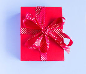 Red gift box with red ribbon isolated on blue background. Top view.