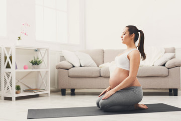 Happy pregnant woman training yoga in hero pose