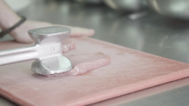 Chef tenderizes pork on cutting board, close up