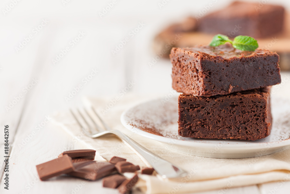 Wall mural chocolate brownie square pieces in stack on white plate decorated with mint leaves and cocoa powder 