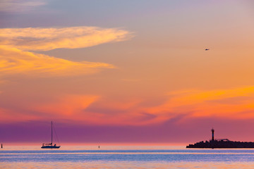 Naklejka na ściany i meble Summer bright orange purple sunset with a helicopter in the clouds and the silhouette of a sailing boat next to a lighthouse on the shore. Coastal seascape on the Black Sea, Sochi, Russia.