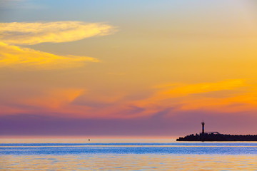 Fototapeta na wymiar Summer bright orange sunset with clouds in the sky and silhouette of a lighthouse on the shore. Coastal seascape on the Black Sea, Sochi, Russia.