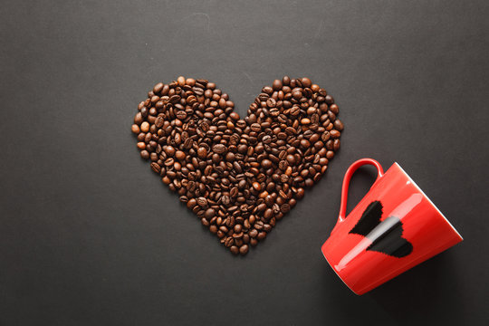 Brown coffee beans in form of heart with red cup for tea with hearts isolated on black texture background for design. Saint Valentine's Day card on fabruary 14, holiday concept.