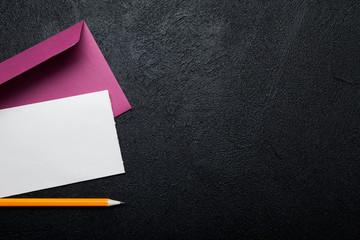 Pink envelope, blank white sheet of paper and pencil on black background. Empty space for text.