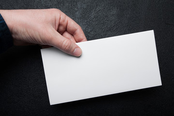 Standard white blank of mail envelope in hand on a black background. Mock up.