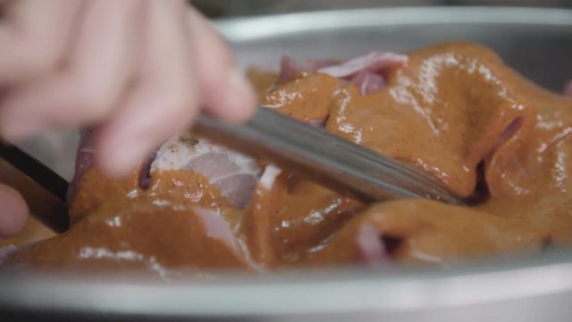 Slow motion close up, chef mixes mojo sauce with pork