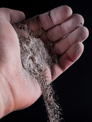 Gray ash pour out of human hand isolated on black. Close up. Selective focus
