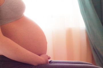 closeup of hands holding the cute belly of a pregnant woman on the ninth month. against the...