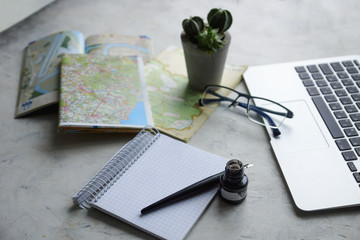 Summer vacations planning. Laptop computer, old map, pot plant, notebook and glasses on light background