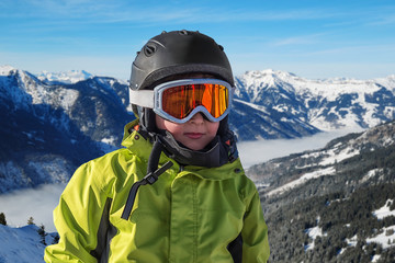 Fototapeta na wymiar Portrait of boy in helmet and ski goggles on a sunny day in the mountains. Active outdoor childhood concept