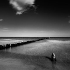 zonsondergang over de zee met een houten pier, zwart-wit foto, lange blootstelling