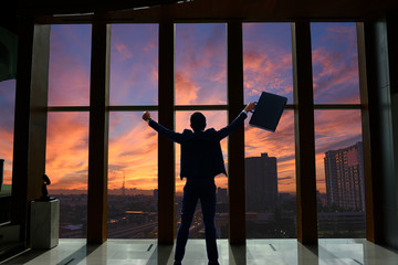 Fototapeta na wymiar silhouette of businessman with document bag in hand raise arms up because success in business over sunrise sky background