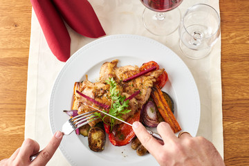 Man cutting a grilled chicken in a restaurant with vegetables