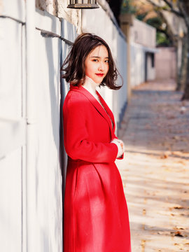 Beautiful young brunette woman wearing a red coat in autumn city. Outdoor fashion portrait of glamour young Chinese cheerful stylish lady in street. Emotions, people, beauty and lifestyle concept.