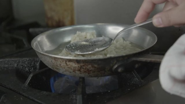 Chef spreads rice in stovetop pan, close up