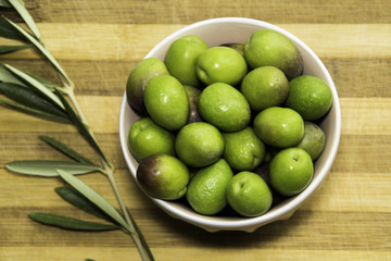 Plate of Green olives and leaves ready to eat in chopping board background.