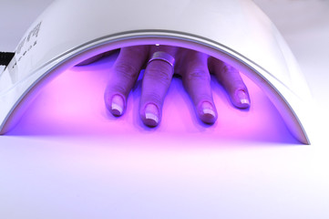 Manicure with uv led lamp, curing gel or hybrid varnish, manicure on table. Hand of a woman under the lamp - obrazy, fototapety, plakaty