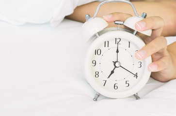Closeup woman hand turn off alarm clock on white bed in the morning for wake up time concept