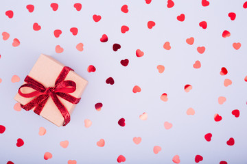 Craft box with red ribbon bow and glitter heart confetti. Valentine day concept. Trendy minimalistic flat lay design background