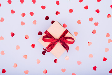 Craft box with red ribbon bow and glitter heart confetti. Valentine day concept. Trendy minimalistic flat lay design background