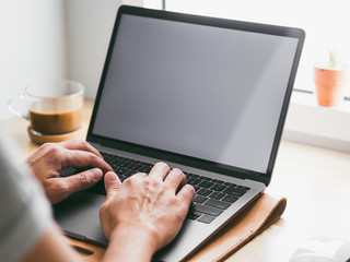 Man working on his laptop by the windows with white monitor.