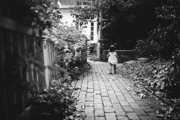 Little Girl Walking Along Brick Path in Beautiful Garden