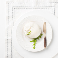 Italian cheese Burrata (mozzarella) with a vintage knife and fresh arugula on a white plate and a wooden light background. Flat lay, top view