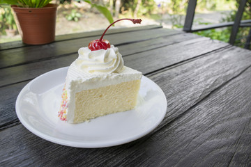 Piece of butter cake with cream and Cherry on dark wood table in cafe.
