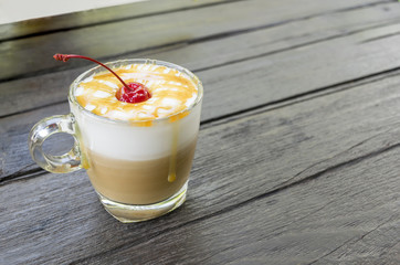 Coffee with milk foam topped with caramel sauce and cherries on dark wood table in cafe.