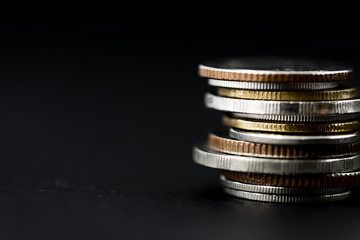 Closeup of coins stack isolated on black background - obrazy, fototapety, plakaty