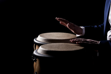 Hands of a musician playing on bongs in dark tones