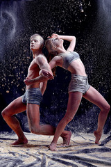 Athletic girl and the man are in the form of gymnastic sports figures with thrown flour on black background