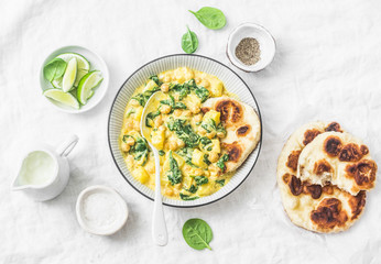 Chickpeas, spinach, potato curry plate and naan flatbread on white background, top view. Indian healthy vegetarian food