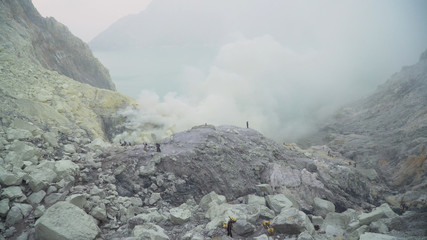 Fototapeta premium Extraction of sulfur in the crater of a volcano. Sulfur, sulfur gas, smoke. Kawah Ijen, crater with acidic crater lake where sulfur is mined. Ijen volcano complex is a group of stratovolcanoes in the