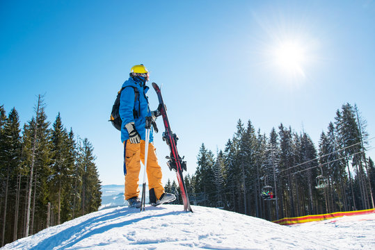Full length shot of a skier standing on top of a snowy slope in the mountains looking around enjoying beautiful sunny winter day. Winter resort