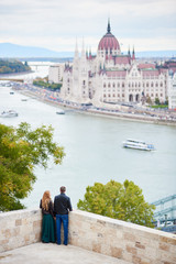 Naklejka premium Elegant pair is enjoying each other on the background of Danube River and Parliament Building in Budapest, Hungary. Blurred background