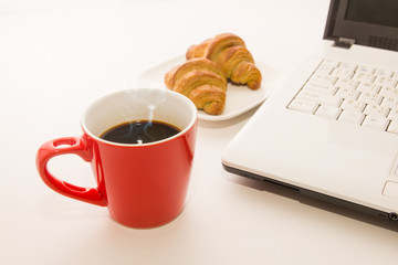 Laptop  with coffee cup and croissant on the table