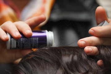 Female hand puts powder for volume on dark hair, close-up.