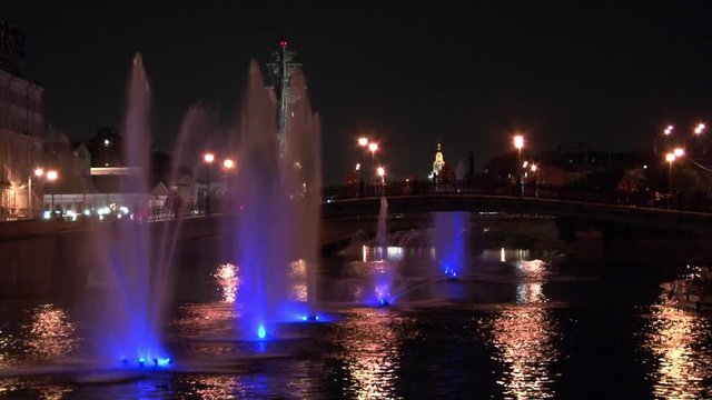 Glowing fountains in river and lanterns on bridge background in Moscow at night. Beautiful views of capital of Russia. Bright colorful streets and city Lights