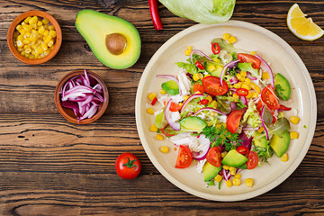 Appetizing vegan salad from tomatoes, avocado, corn, red onion and lettuce leaves.Tasty vegan food. Healthy vegan food. Vegetarian salad.Top view