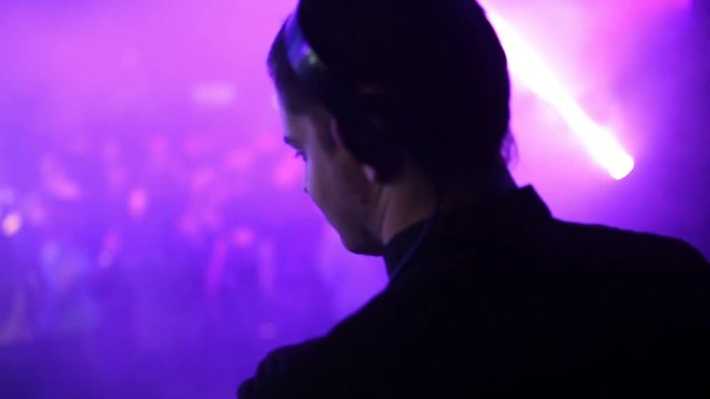 Back view. The back and headphones of the DJ in the foreground, the dancing people are blurred.