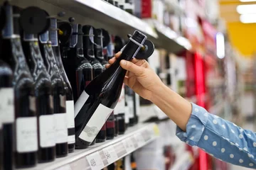 Crédence de cuisine en verre imprimé Bar Woman is buying a bottle of wine in supermarket background