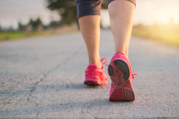 Close up sneaker of athlete woman runner feet on rural road while running exercise on sunset background