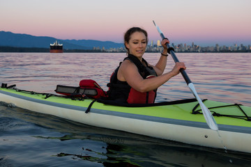 Middle Age Caucasian Woman Kayaking on a Sea Kayak during Sunset with City Skyline in Background. Taken in Vancouver, BC, Canada.