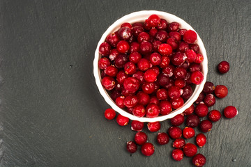 Frozen berries of cranberries in white bowl on black stone