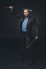 man in suit with dual katana swords looking at camera on black