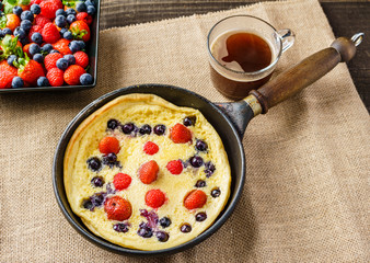 Fresh homemade dutch baby pancake with blueberry raspberry and strawberry in a pan on a table.